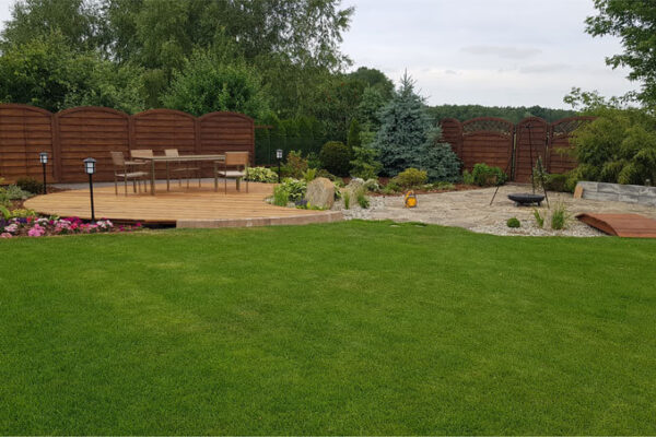 Efekt modernizacji ogrodu przydomowego na bazie naszego projektu ogrodu. Nowoczesna aranżacja ogrodu z tarasem, miejscem na palenisko i oświetleniem.